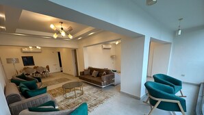 A spacious living room with a sofa set, a coffee table, and a rocking chair. There is a dining area in the background with a table and chairs. - Luxury Flat Stunning Nile View (Giza)