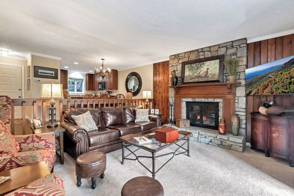 A living room with a stone fireplace, leather sofa, and a dining area with wooden cabinets. - Willow 2 | Fireplace, Restaurant, Pool, Spa (Blowing Rock)