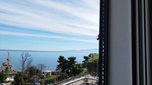 Une vue depuis une fenêtre donnant sur une étendue d’eau, avec des montagnes lointaines, un ciel dégagé et quelques zones verdoyantes.