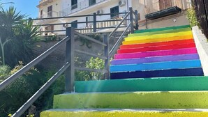 Un escalier extérieur, avec une rampe aux couleurs de l’arc-en-ciel, mène à un immeuble doté de balcons et de climatiseurs.