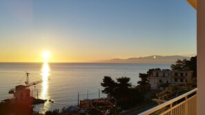 Une vue côtière avec un coucher de soleil sur la mer, des bâtiments et une structure de grue.