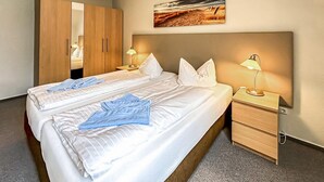 A hotel room with a large bed, two bedside tables with lamps, a wooden wardrobe, and a painting on the wall. - Ferienwohnung Trassenheide (Trassenheide (Ostseeba)
