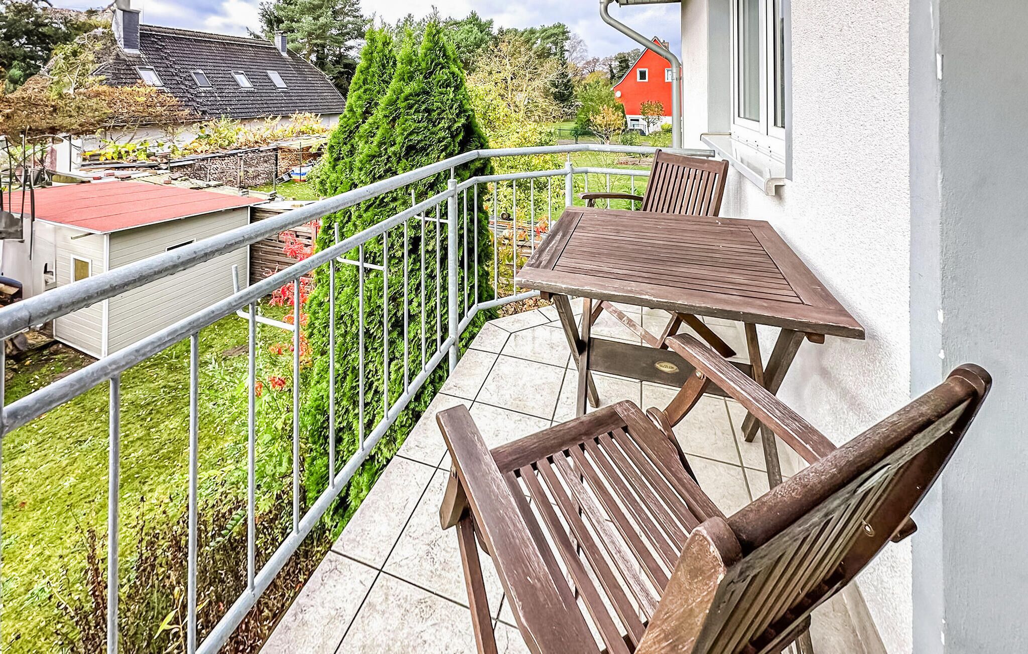 Een balkon met een houten tafel en twee stoelen, omringd door een metalen hekwerk.