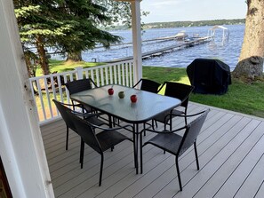 Une terrasse extérieure couverte, dotée d’une table et de chaises, qui offre une vue sur un lac avec des quais et une zone abritée.
