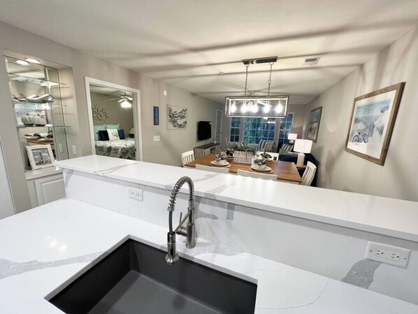 A modern kitchen with a large island, a built-in sink, and a dining area in the background.