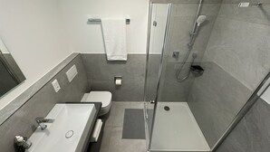 A modern bathroom with a glass-enclosed shower, a sink with a mirror, and a toilet. - 35qm Serviced Apartment (Töging am Inn)