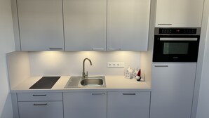 A modern kitchen with white cabinets, a stainless steel sink, a built-in oven, and a black induction cooktop. - 35qm Serviced Apartment (Töging am Inn)