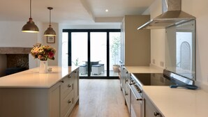 A modern kitchen with a large island, stainless steel appliances, pendant lighting, and a view to an outdoor seating area.