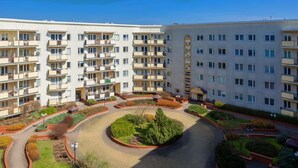 Um edifício residencial com vários andares, varandas, área ajardinada central e acesso por uma entrada circular.
