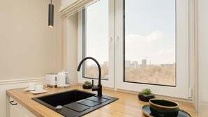 Cozinha moderna com pia preta, bancada de madeira e vista da cidade através de amplas janelas.