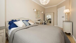 Quarto com cama, mesas de cabeceira, escrivaninha, cadeira, espelho e lustre.