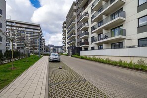 Un edificio de apartamentos moderno con balcones, un sendero pavimentado y un coche estacionado en la calle.