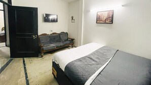 Une chambre avec un lit, un canapé, une télévision et un tableau au mur.