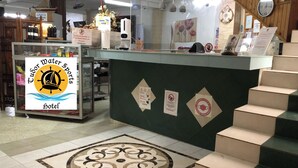 Un hall d'accueil d'hôtel avec une enseigne indiquant « Tudor Water Sports Hotel », une vitrine, un motif décoratif sur le sol et un escalier.