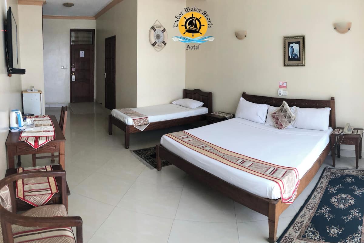 A hotel room with two single beds, a large bed, a desk with a chair, a small table, and a TV.