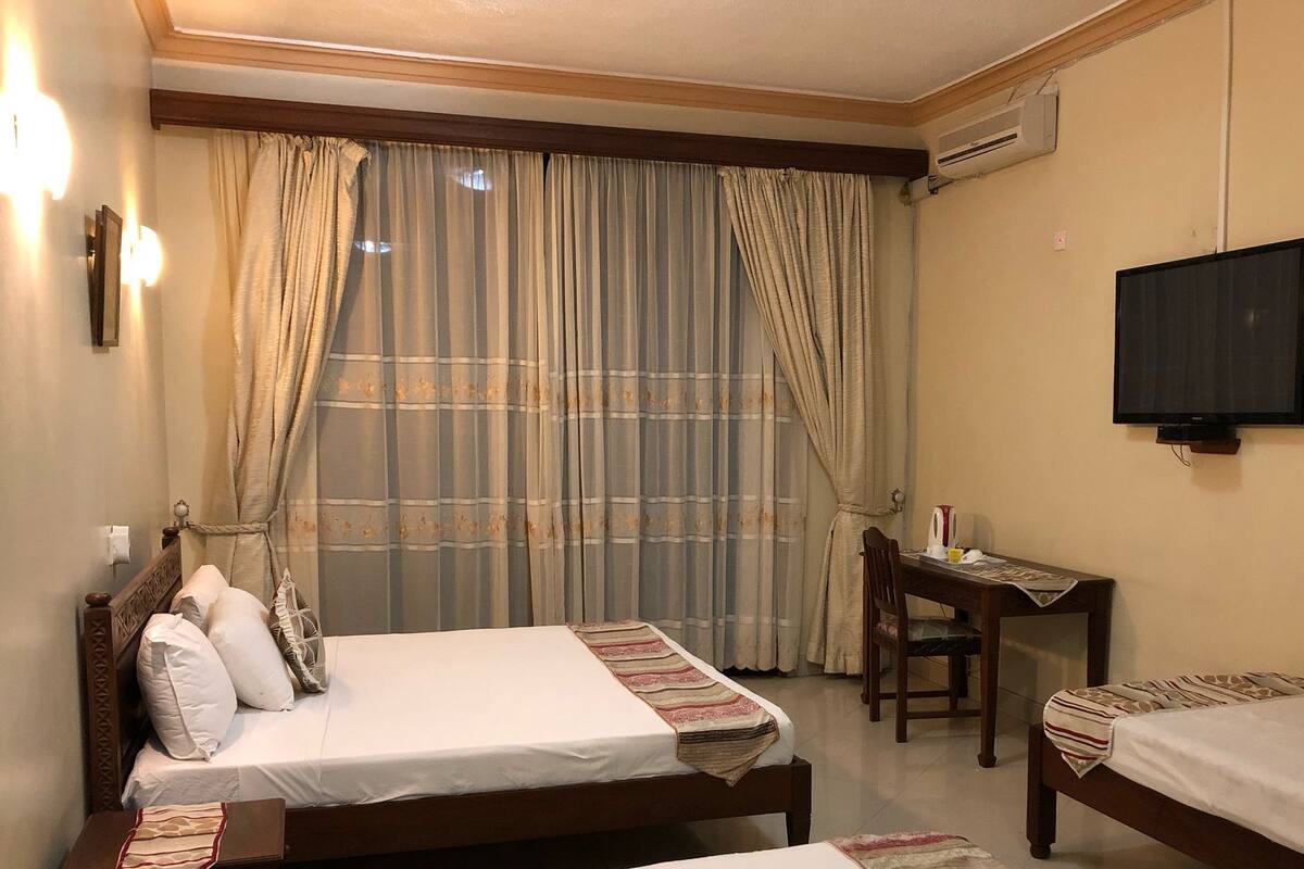 A hotel room with two single beds, a desk, a chair, a television, and a window with curtains.