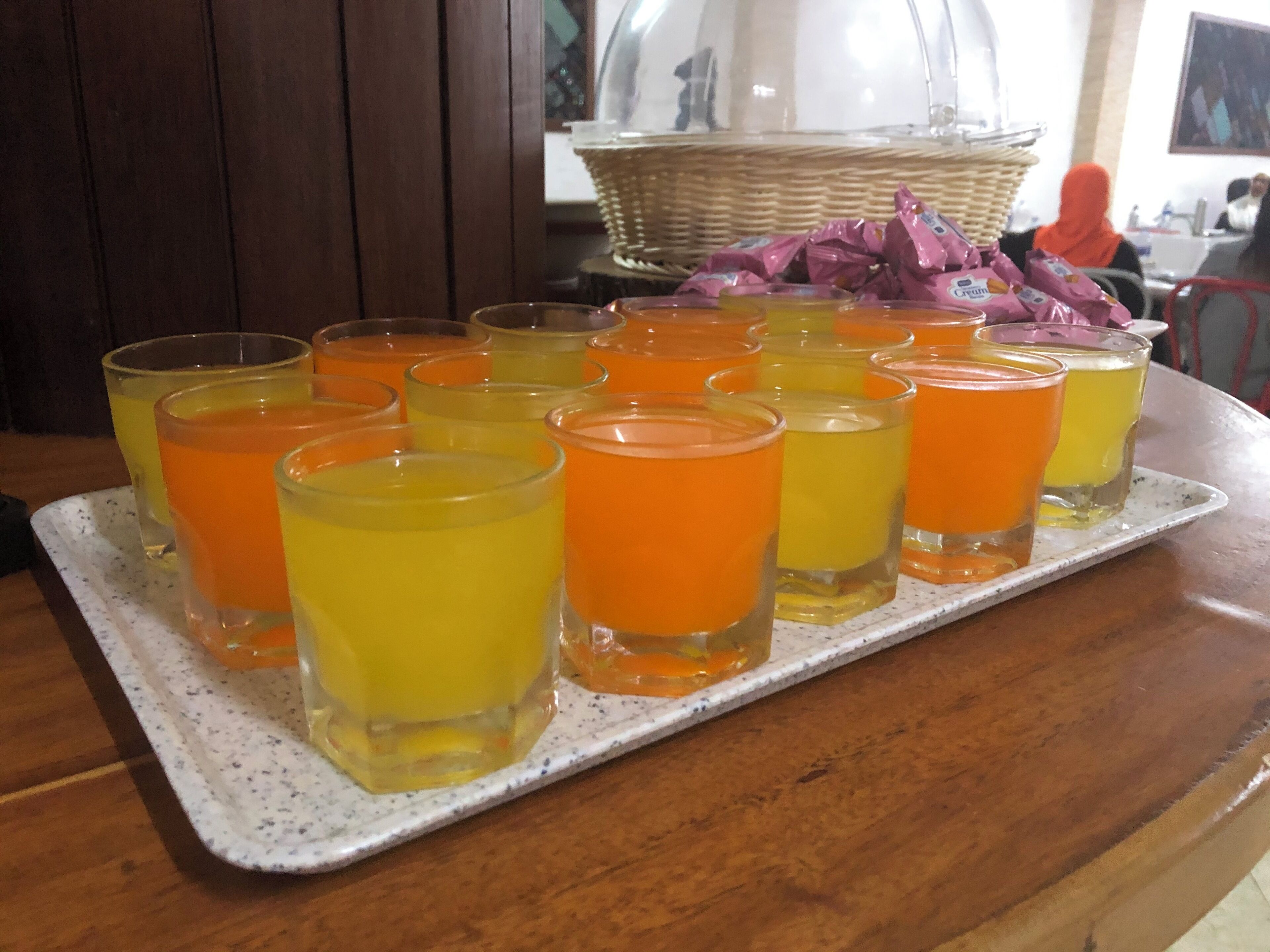 A tray of orange and yellow drinks on a wooden table.