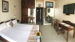 Une chambre d’hôtel avec un grand lit, un bureau avec des chaises, une télévision et une porte donnant sur une salle de bain.