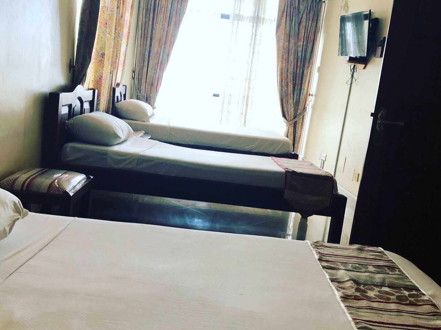 A hotel room with two beds, a bedside table, a lamp, and a window with curtains.