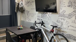 A room with a dining table, chairs, a TV mounted on the wall, and a bicycle leaning against the wall.