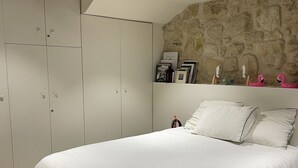 A bedroom with a large bed, white wardrobe, stone wall, and wooden beams.