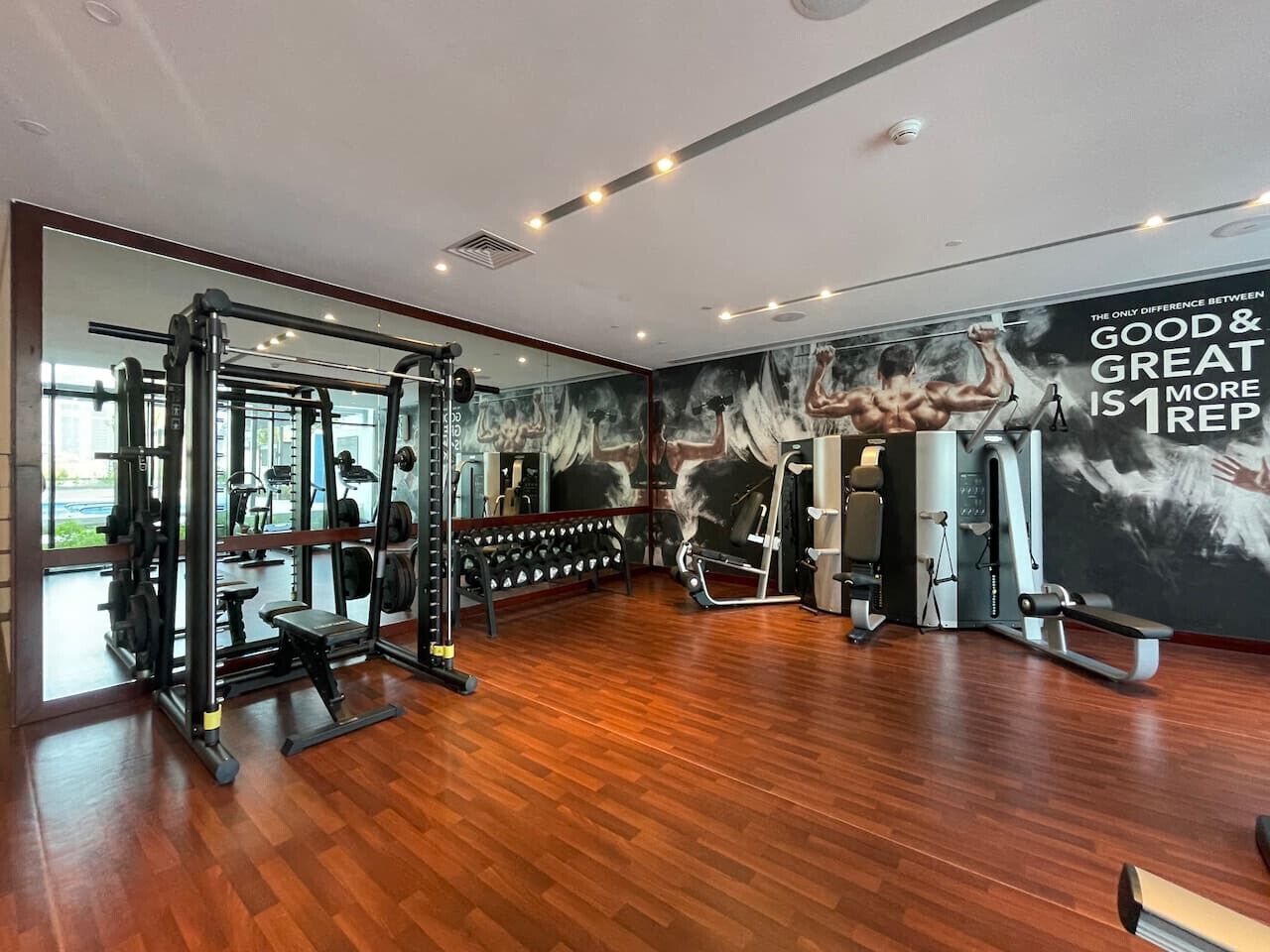 Une salle de sport dotée d’un plancher en bois, d’équipements d’haltérophilie et d’une affiche motivante au mur.