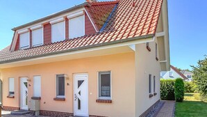 Una casa de dos pisos con techo de tejas rojas, fachada color crema y un pequeño jardín delantero.