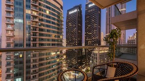 A balcony with wicker chairs and a potted plant, overlooking a cityscape with modern buildings and a clear sky. - World Class | 2BR | Dubai Skyline & Sea view (Downtown)