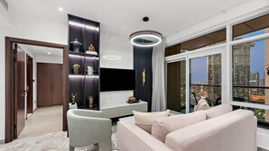 A modern living room with a sofa, armchair, and a coffee table. There is a TV mounted on the wall and a large window with a city view. - World Class | 2BR | Dubai Skyline & Sea view (Downtown)