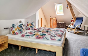 A bedroom with a bed, pillows, a chair, a small table, and a window.
