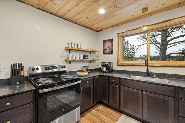 A modern kitchen with dark wood cabinets, a stainless steel stove, and a large window offering a view of trees.