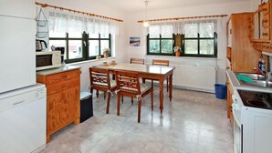 Een praktische keuken met een eettafel, houten stoelen, een magnetron en een fornuis.