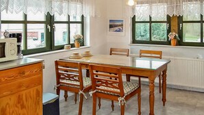 Een keuken met een houten tafel en stoelen, een raam met uitzicht op groen, en een radiator.