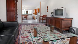 Een woonkamer met een bank, een glazen salontafel, een televisie en een keuken op de achtergrond.