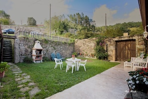 A stone wall, a wooden gate, a stone staircase, a white table with chairs, and a potted plant.