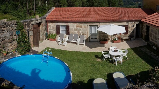 A stone house with a red-tiled roof, a swimming pool, and outdoor seating.
