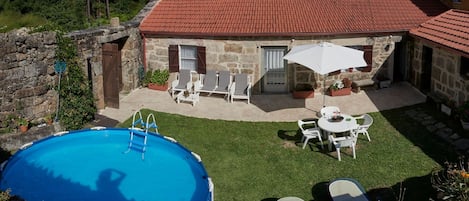 A stone house with a red-tiled roof, a swimming pool, and outdoor seating.