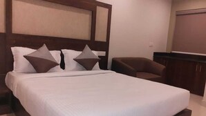 A neatly made bed with a wooden headboard, a brown armchair, and a small desk in a hotel room. - Citi Luxe Hotel (Chennai)