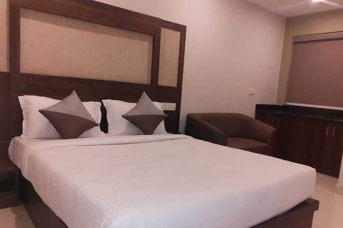 Una cama bien hecha con cabecera de madera, un sillón marrón y un pequeño escritorio en una habitación de hotel.
