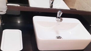 A bathroom with a black countertop, a white sink, and a trash can. - Citi Luxe Hotel (Chennai)