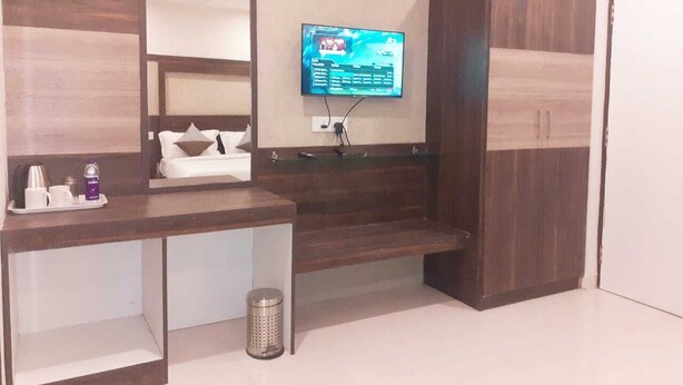 A hotel room with a wooden vanity, a mounted TV, and a wardrobe. - Citi Luxe Hotel (Chennai)