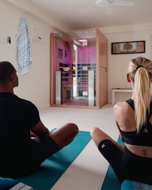 Une pièce avec un tapis de yoga, une personne assise et une porte donnant sur une autre pièce.