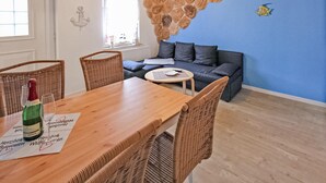 Un salon chaleureux avec une table à manger en bois, des chaises en osier, un canapé gris et un mur en pierre.