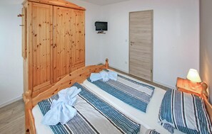A bedroom with a wooden wardrobe, a bed with striped bedding, a television on the wall, and a door. - Ferienhaus Zinnowitz (Seebad) (Zinnowitz (Seebad))