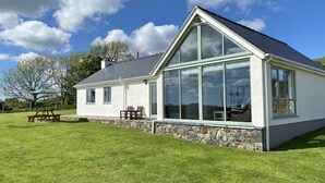 A house with a large glass window, a stone foundation, and a grassy lawn. - Beautiful, Private Farm Cottage in Anglesey (Pentraeth)