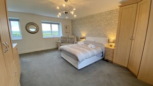 A bedroom with a large bed, a chair, a wardrobe, and a chandelier. - Beautiful, Private Farm Cottage in Anglesey (Pentraeth)