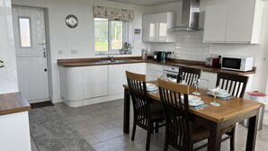 A modern kitchen with white cabinetry, a wooden dining table, and a built-in oven. - Beautiful, Private Farm Cottage in Anglesey (Pentraeth)