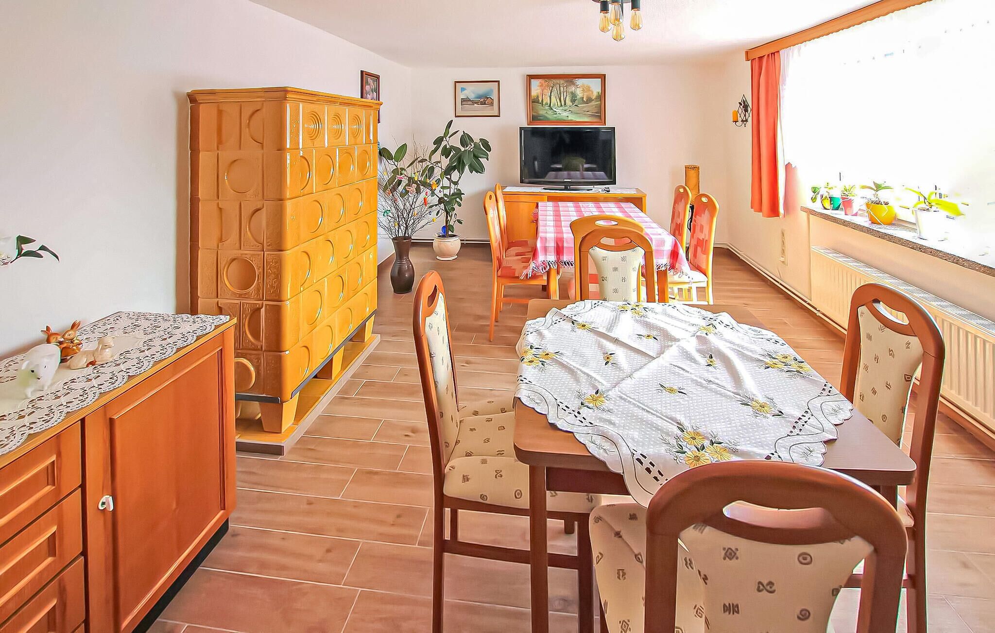 A dining area with a table set for four, surrounded by wooden chairs. A television is mounted on the wall above the table.