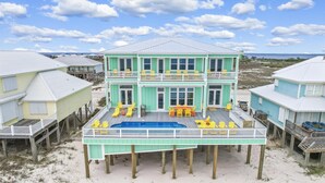Une maison de deux étages située en bord de mer, dotée d’un balcon, d’une piscine et de plusieurs chaises.