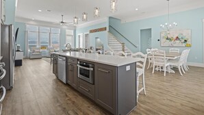 Une cuisine spacieuse dotée d’un îlot central, un coin repas avec des chaises blanches et un escalier menant à un deuxième étage.